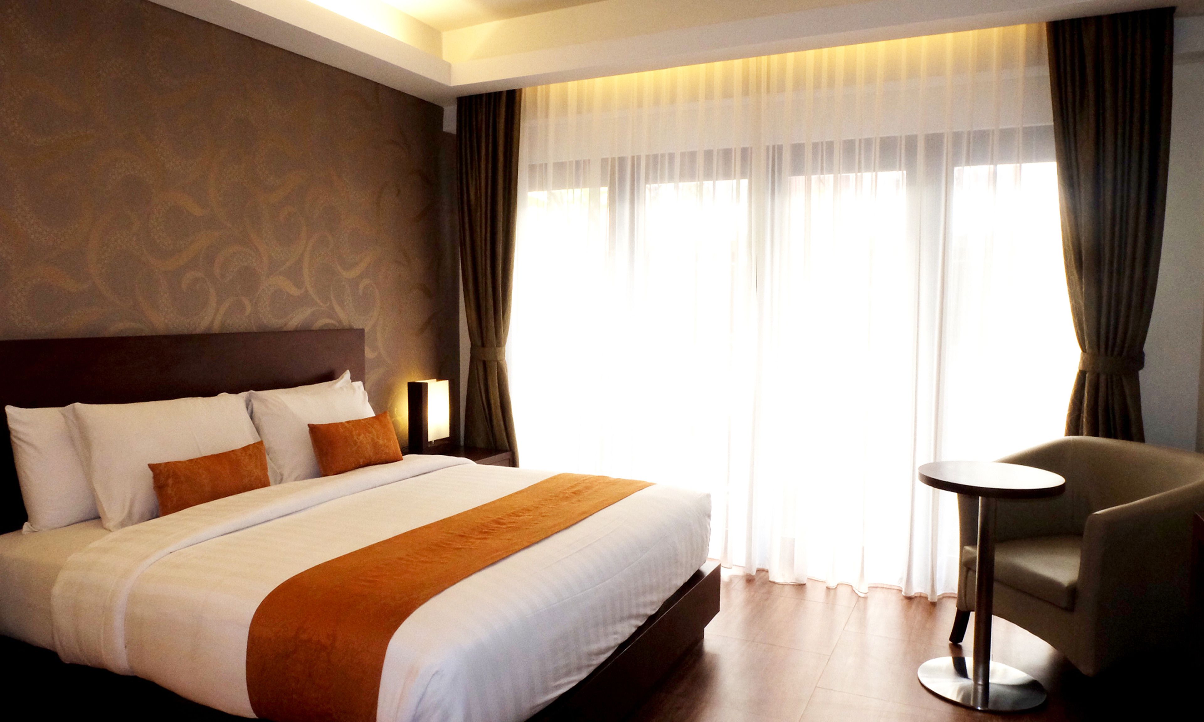 A hotel room with a large bed, a bedside table, a chair, and a window with curtains.