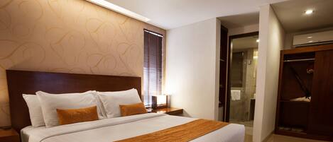 A modern hotel room with a large bed, wooden headboard, and a walk-in closet.