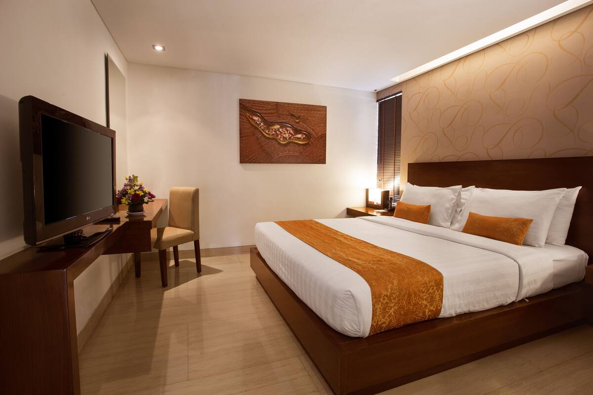 A modern hotel room with a large bed, a flat-screen TV, a desk with a chair, and a decorative wall piece.