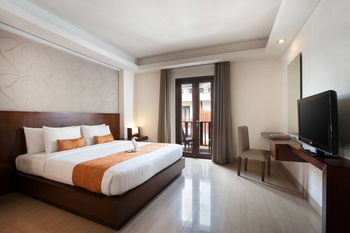 A hotel room with a large bed, a desk with a TV, and a balcony with curtains.
