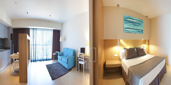 Habitación de hotel con cama, escritorio, sillón, sofá y vista a la ciudad.