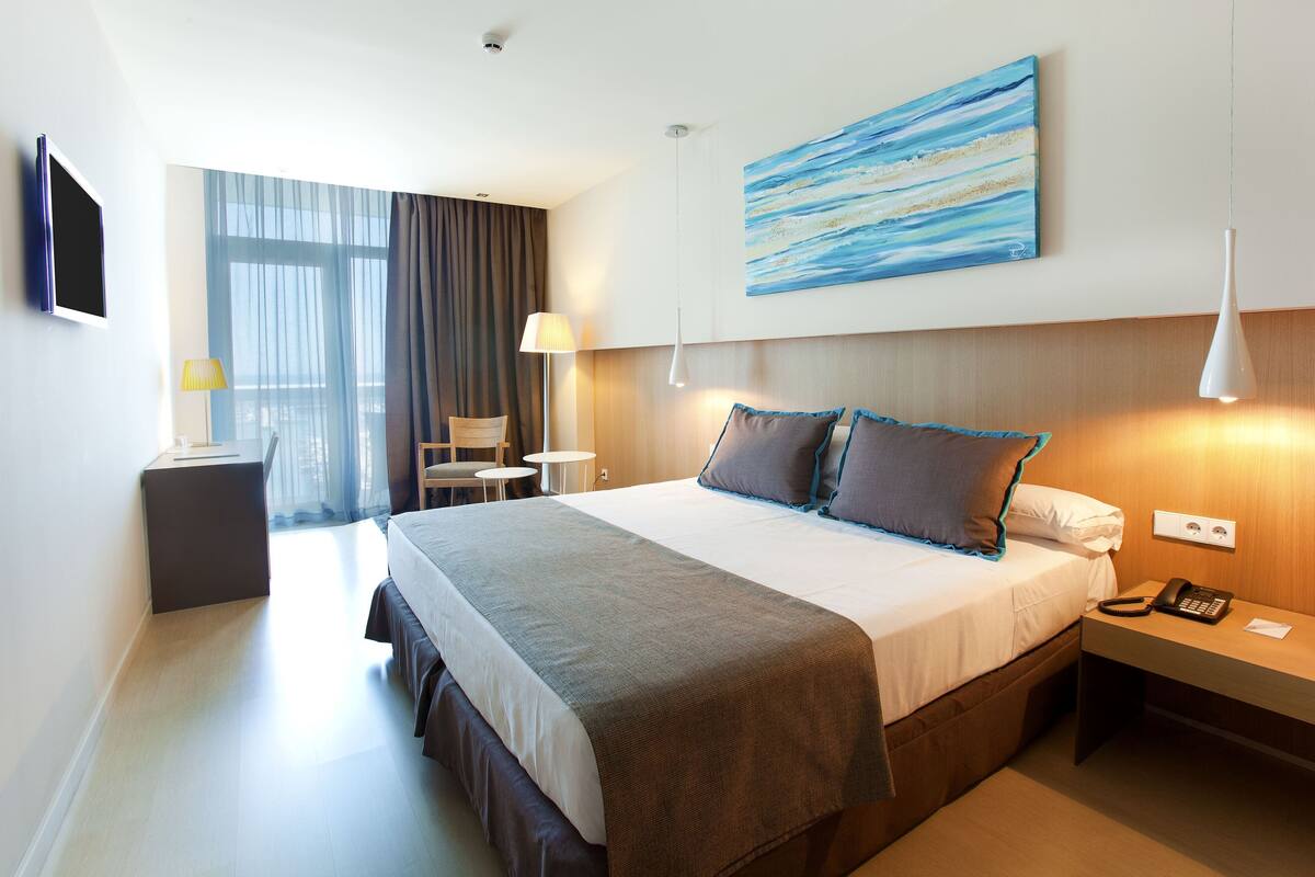 Ein Hotelzimmer mit einem großen Bett, einem Nachttisch, einer Lampe und einem Bild an der Wand.