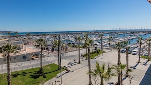 Eine Marina mit zahlreichen vertäuten Booten, Palmen säumen die Promenade, und ein klarer, blauer Himmel.