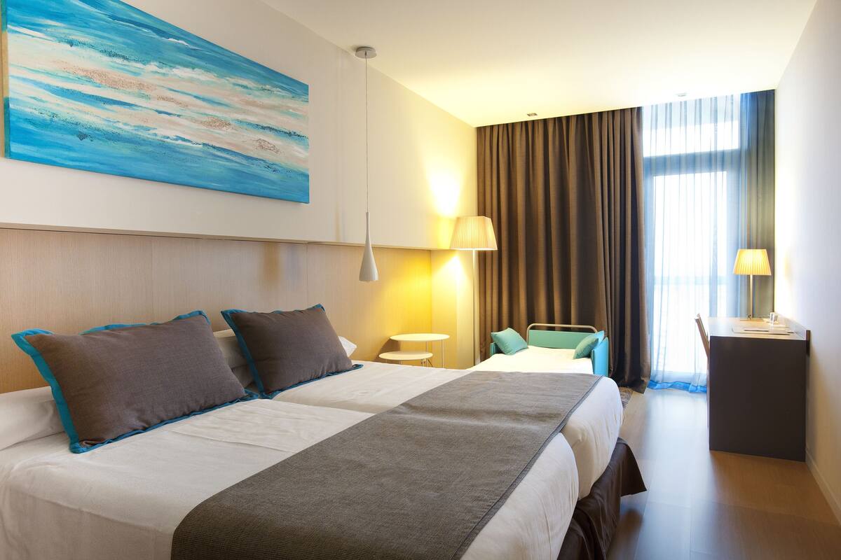 Ein Hotelzimmer mit zwei Betten, einem Schreibtisch, einem Stuhl, einer Lampe und einem Bild an der Wand.