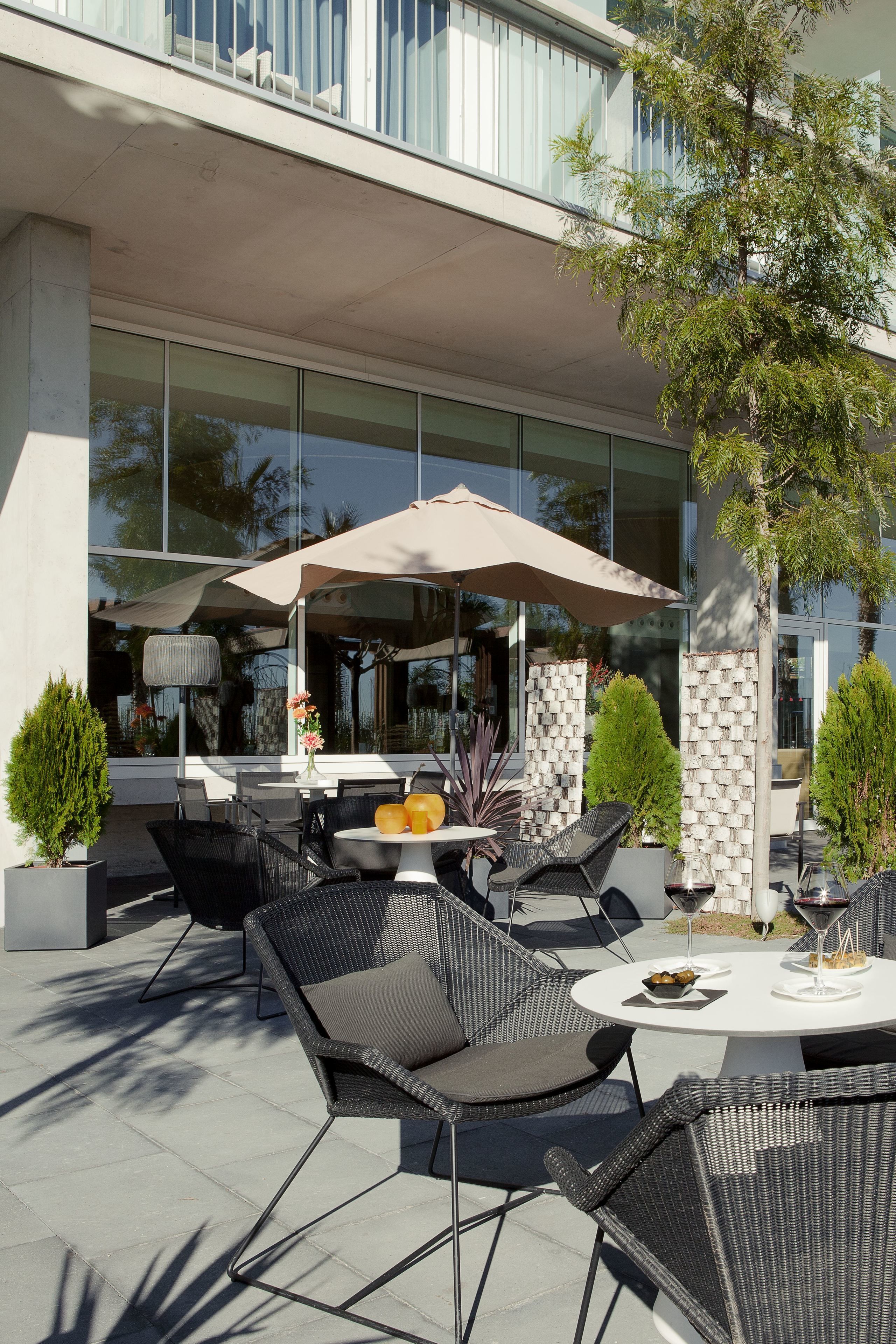 An outdoor seating area with wicker chairs and a round table, a large umbrella, and a potted plant.