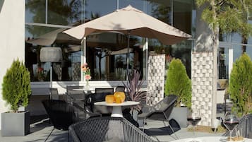 An outdoor seating area with wicker chairs and a round table, a large umbrella, and a potted plant.
