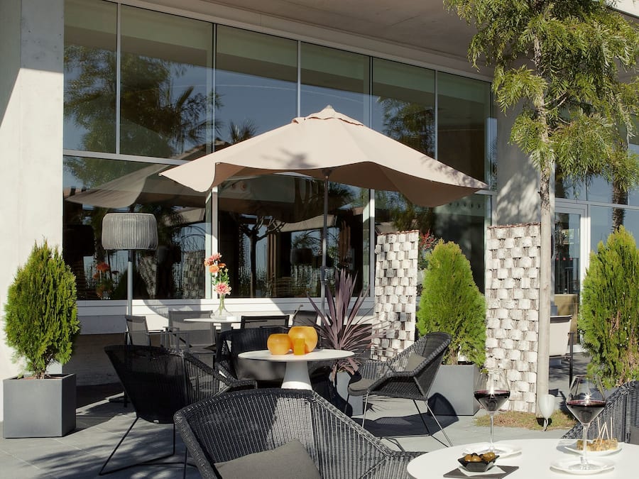 An outdoor seating area with wicker chairs and a round table, a large umbrella, and a potted plant.