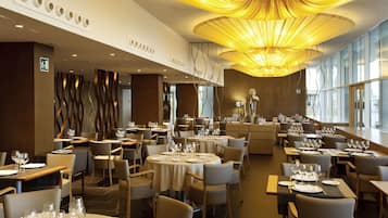 Un restaurante espacioso con varias mesas y sillas, y un moderno candelabro.