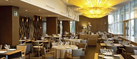 A spacious restaurant with multiple dining tables, chairs, and a modern chandelier.