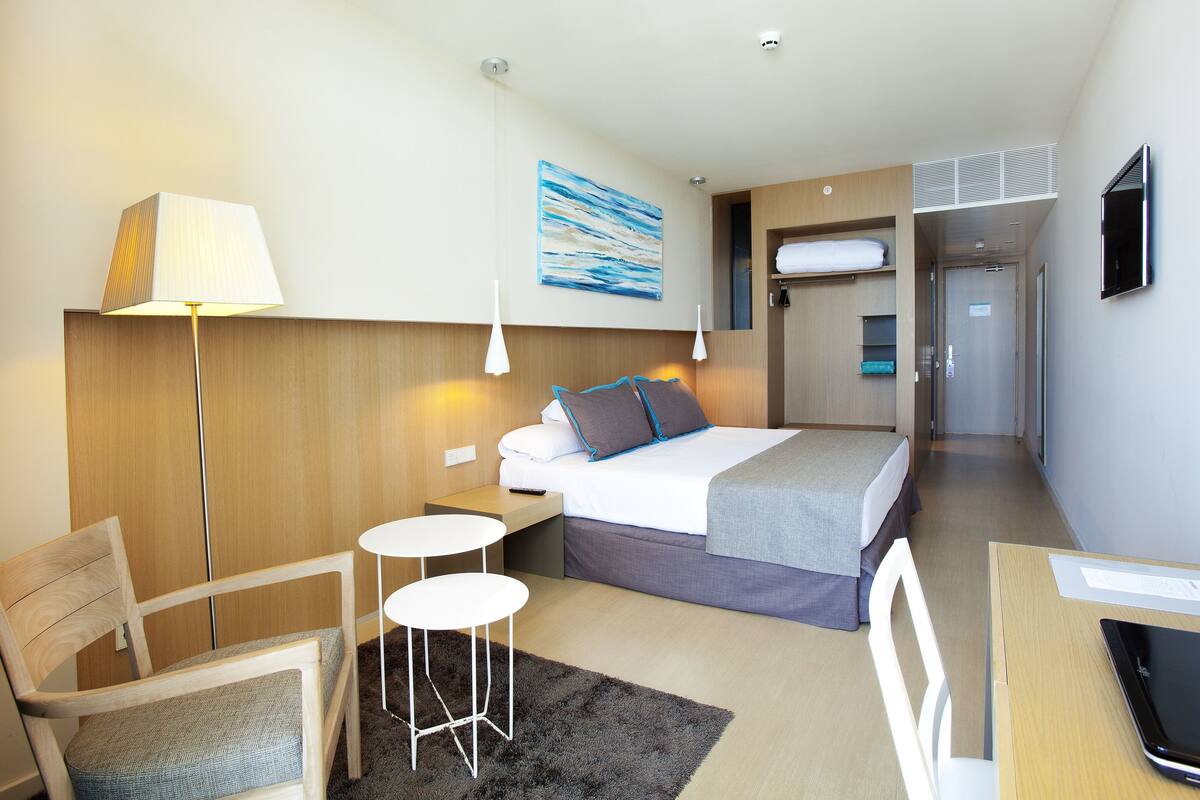 Ein Hotelzimmer mit einem Bett, einem Schreibtisch, einem Sessel, einer Lampe und einem Bild an der Wand.