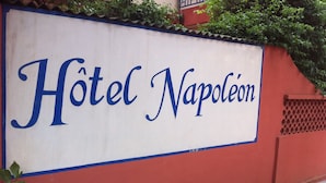 A sign for "Hôtel Napoléon" on a red wall. - Napoléon Aéroport (Lomé)