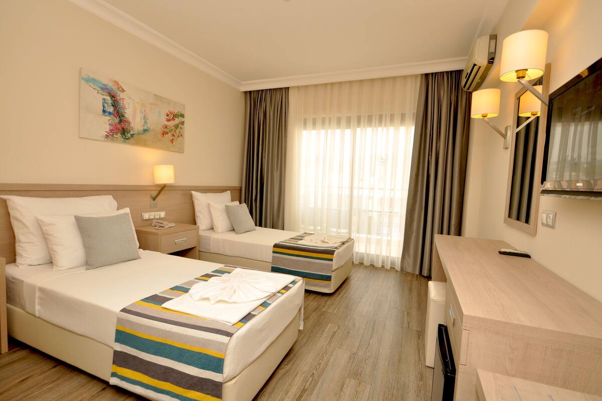 A hotel room with two beds, a desk, a chair, a TV, and a painting on the wall.