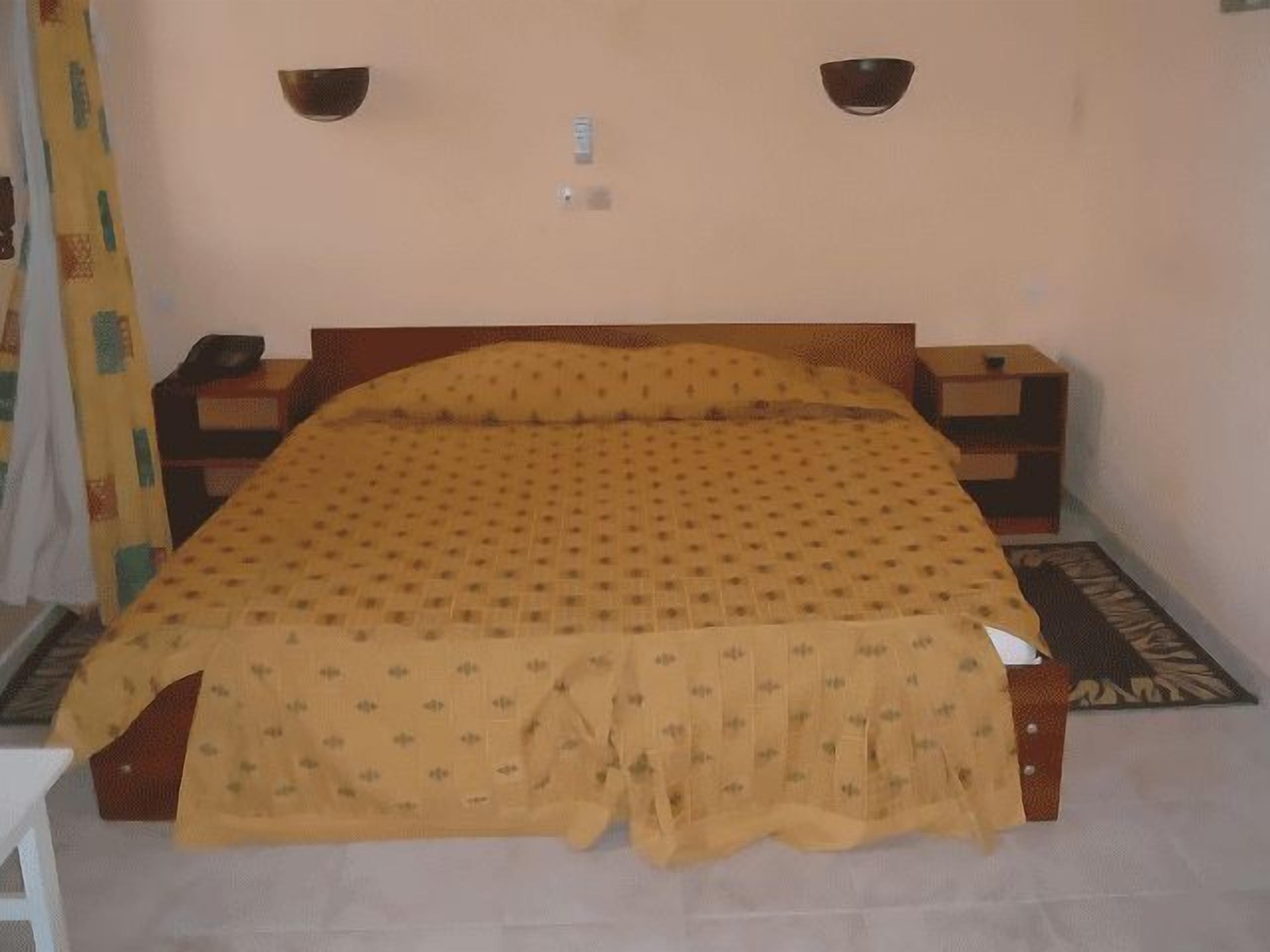 A bed with a patterned bedspread, two bedside tables, and a wall-mounted light fixture.