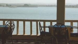 A view from a balcony overlooking a calm body of water with a distant boat, featuring chairs and a railing.