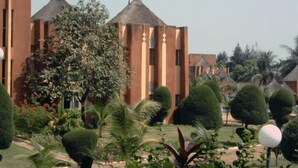 A courtyard with a building featuring a traditional design, including a thatched-roof structure and vertical columns.