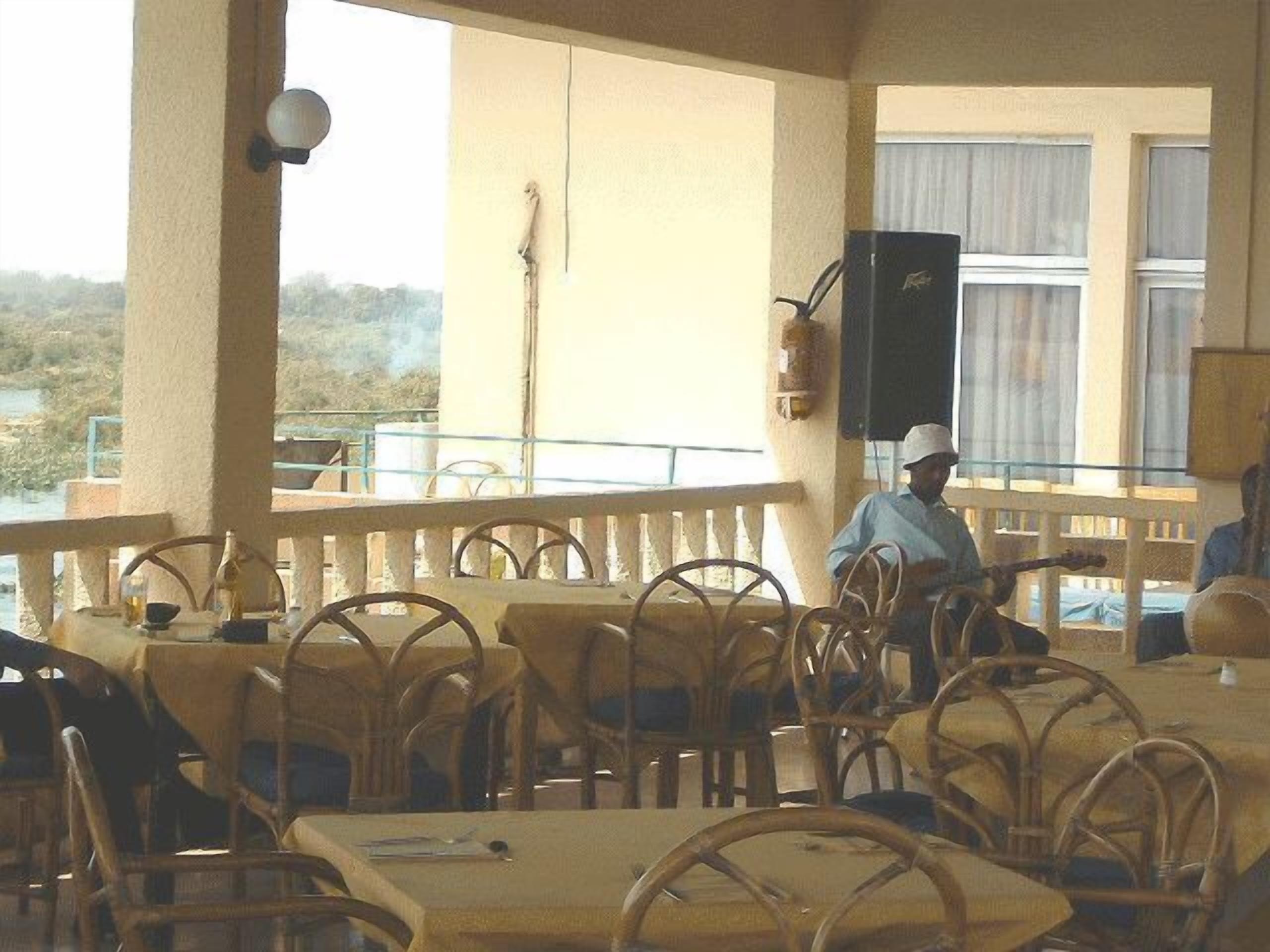 An outdoor dining area with wicker chairs and tables, a person playing guitar, and a view of the landscape.