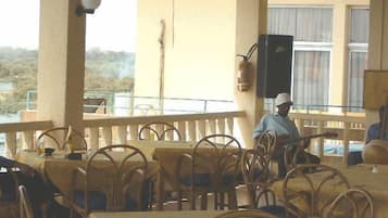 An outdoor dining area with wicker chairs and tables, a person playing guitar, and a view of the landscape.