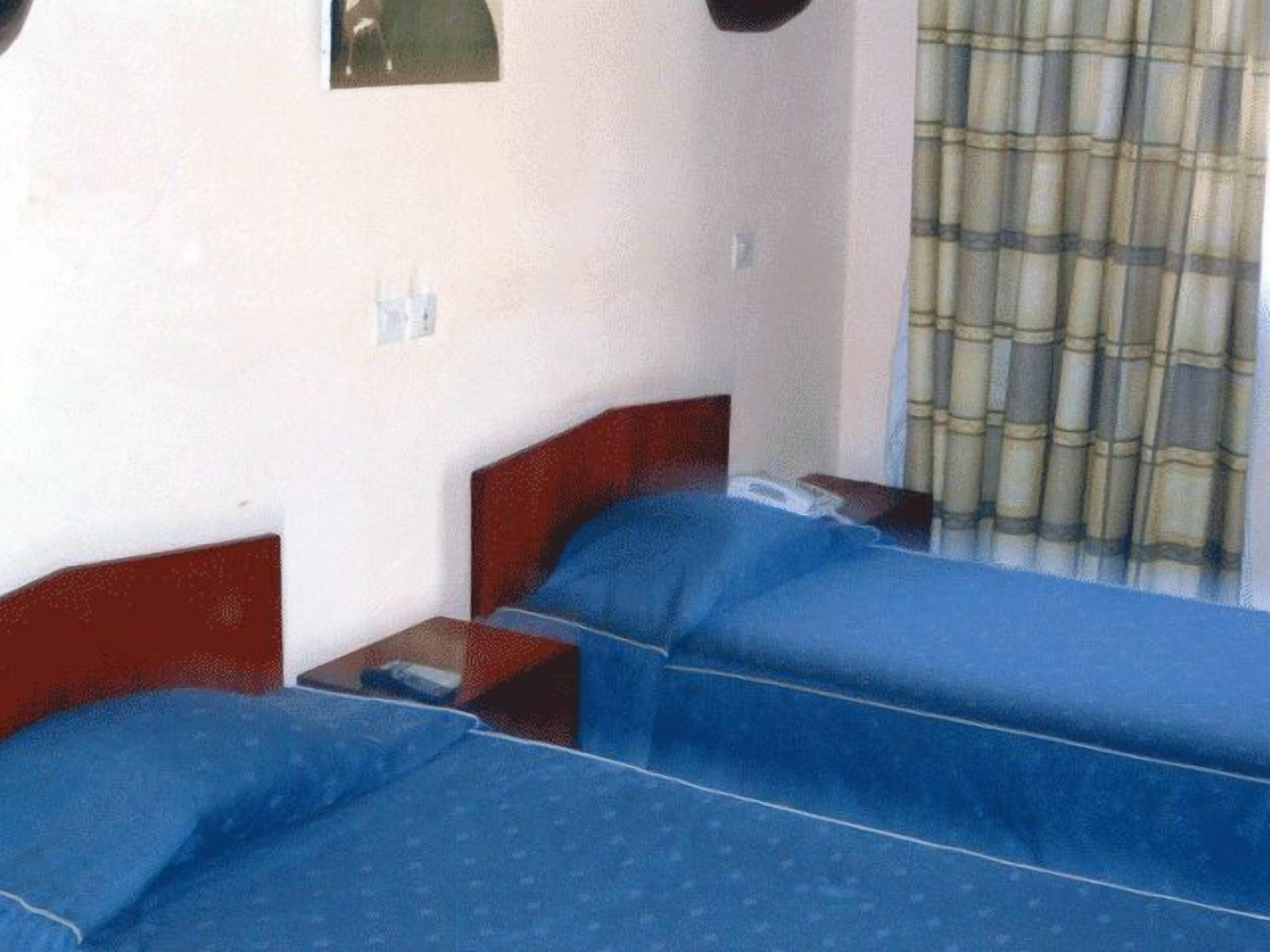 A room with two single beds, a nightstand with a phone, and a window with a curtain.