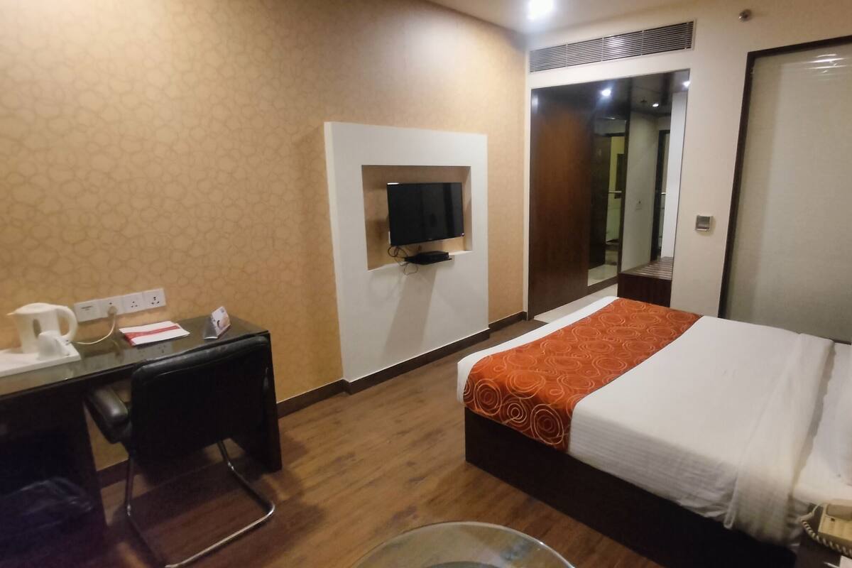 Una habitación de hotel con cama, escritorio, televisión, espejo y lámpara.