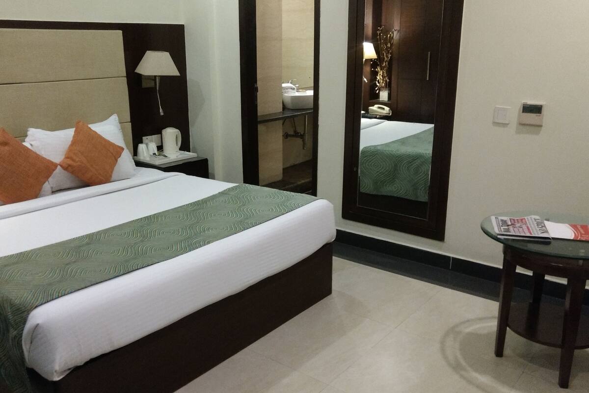 Una habitación de hotel con una cama grande, una mesita de noche, un espejo, una pequeña mesa y una silla.