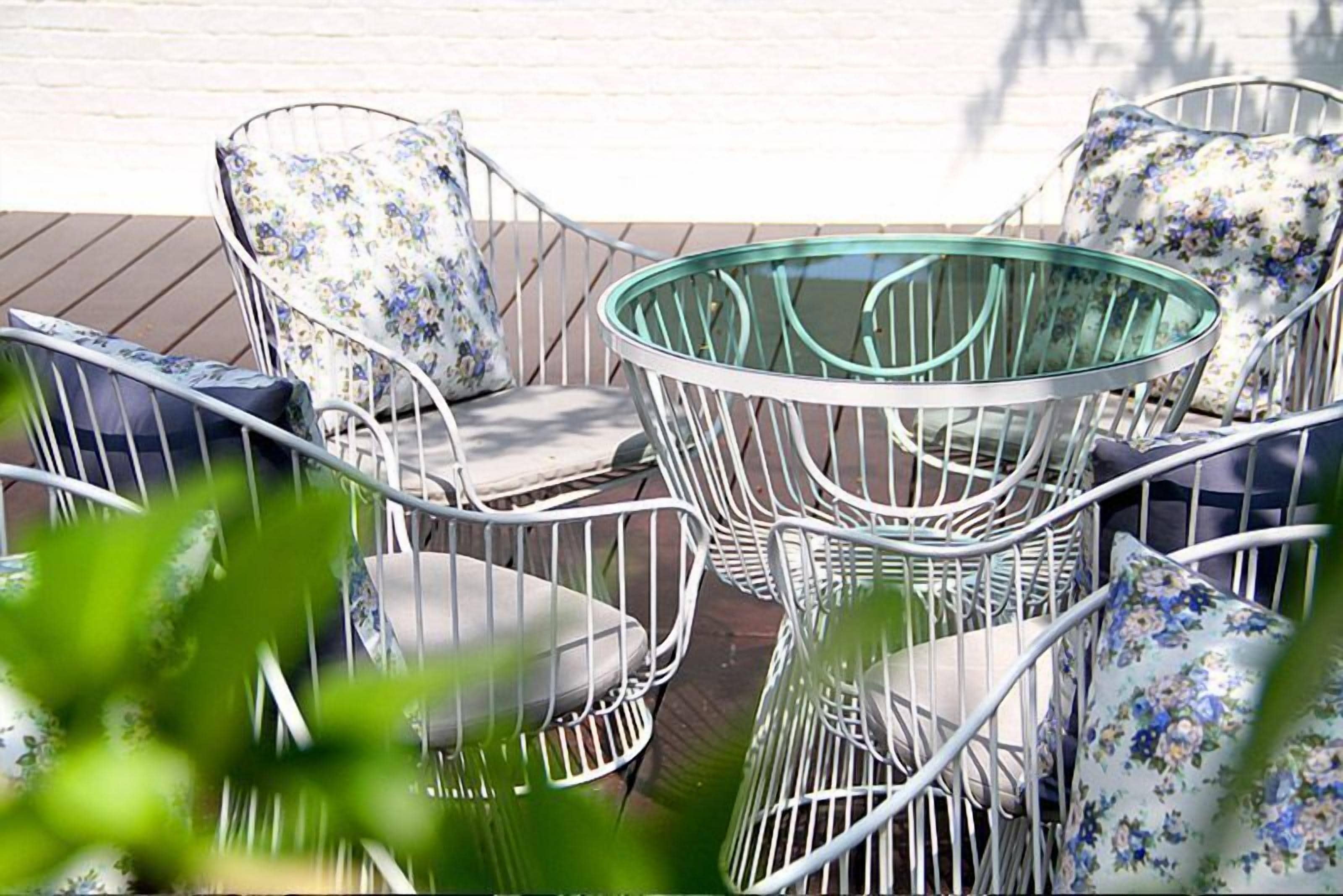 A deck with metal-framed chairs and a glass table, surrounded by a white wall.