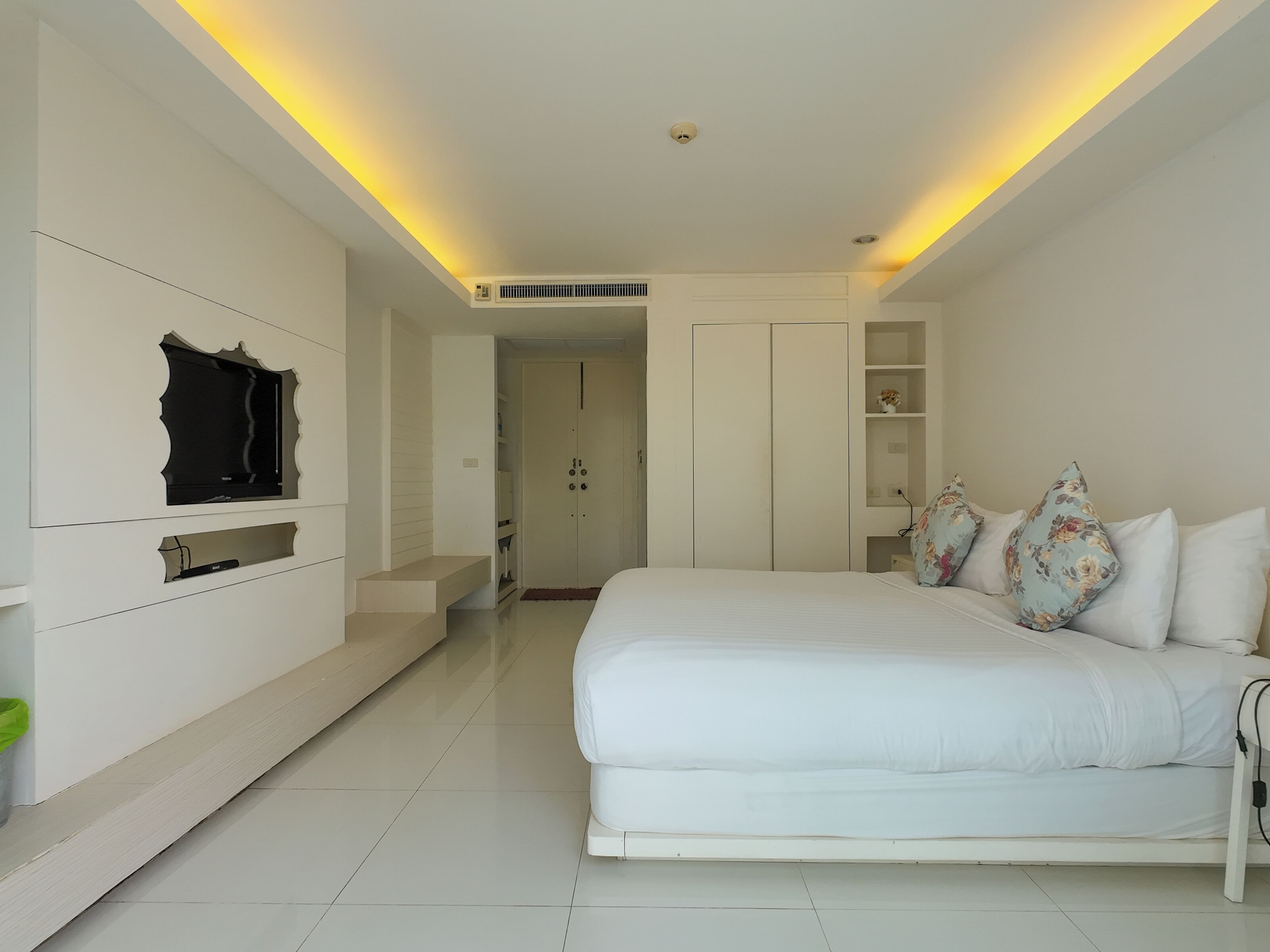A modern bedroom with a large bed, built-in wardrobe, and a flat-screen TV mounted on the wall.