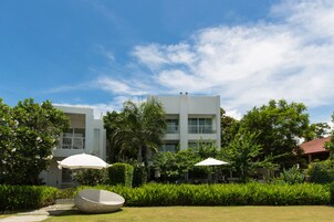 Un hotel moderno con una estructura de dos pisos, rodeado de vegetación exuberante y un cielo azul despejado.