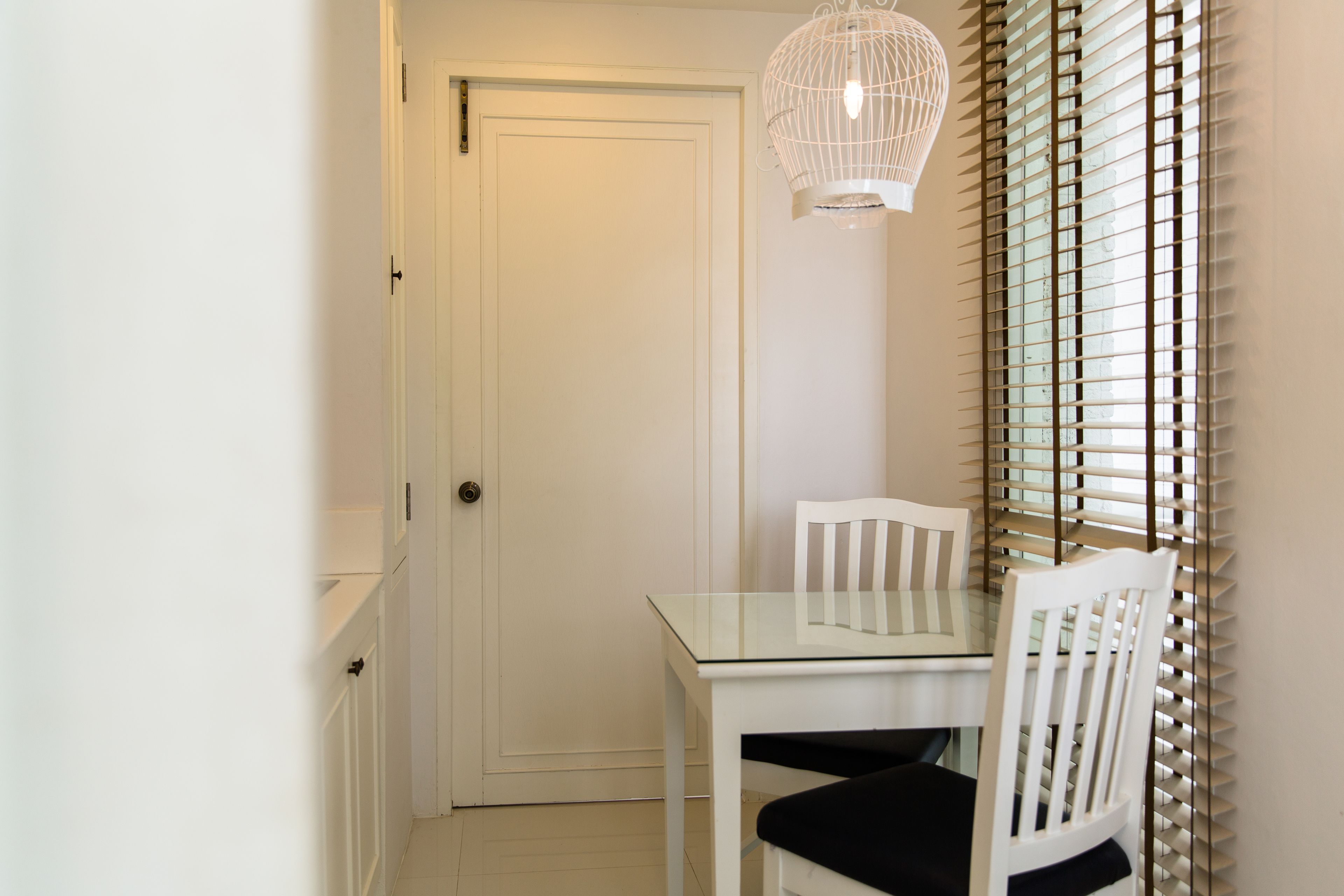 Une porte blanche, une table avec un plateau en verre et une chaise blanche, ainsi qu’une autre chaise blanche avec un coussin noir.