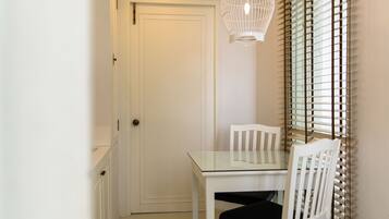Une porte blanche, une table avec un plateau en verre et une chaise blanche, ainsi qu’une autre chaise blanche avec un coussin noir.