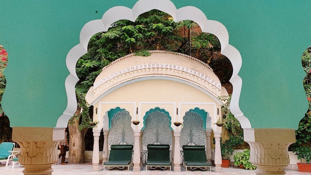 A pool area with a fountain, green lounge chairs, and a decorative archway. - Alsisar Haveli - A Heritage Hotel (Jaipur)