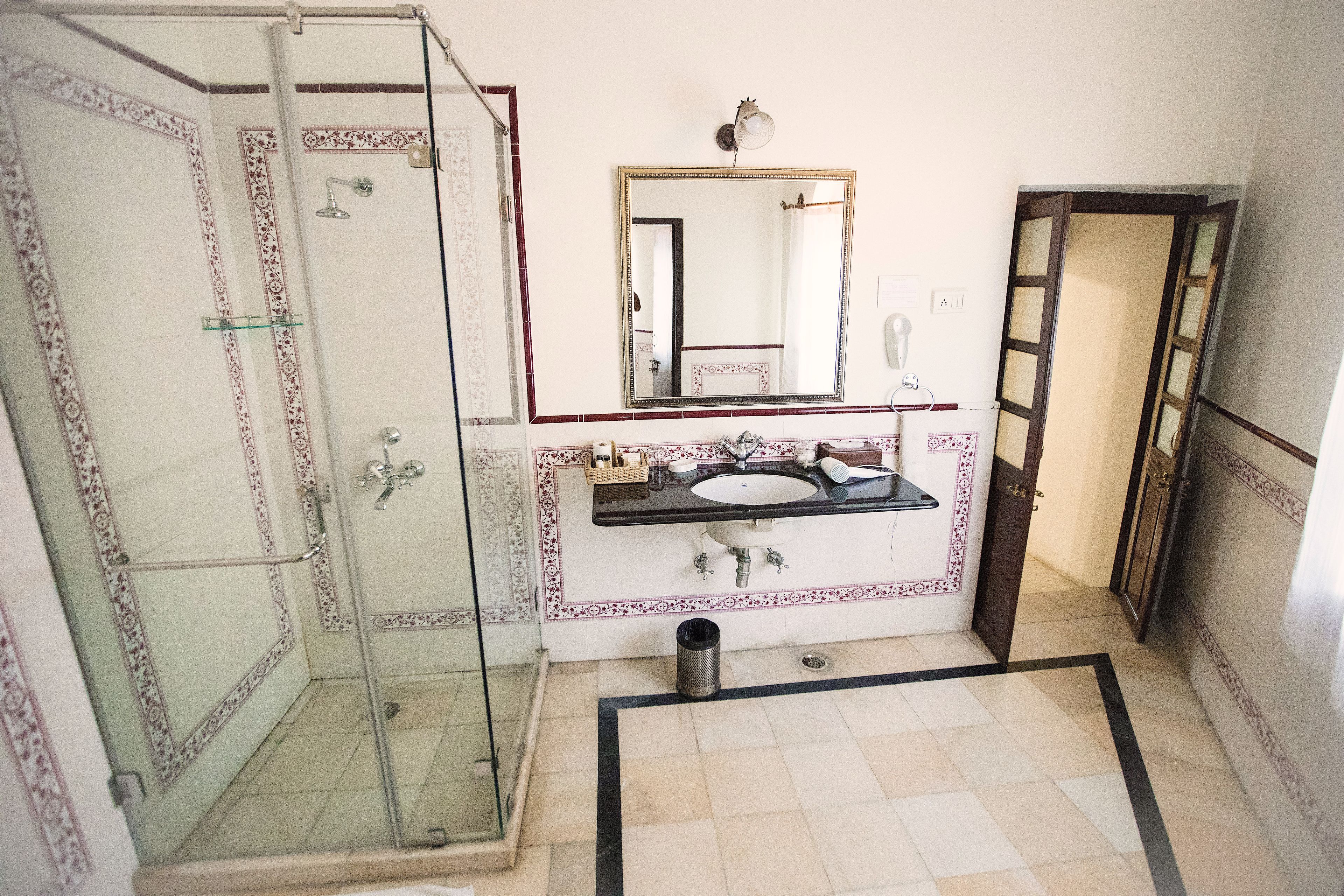 A bathroom with a glass-enclosed shower, a sink with a mirror above it, and patterned tiles on the walls and floor.