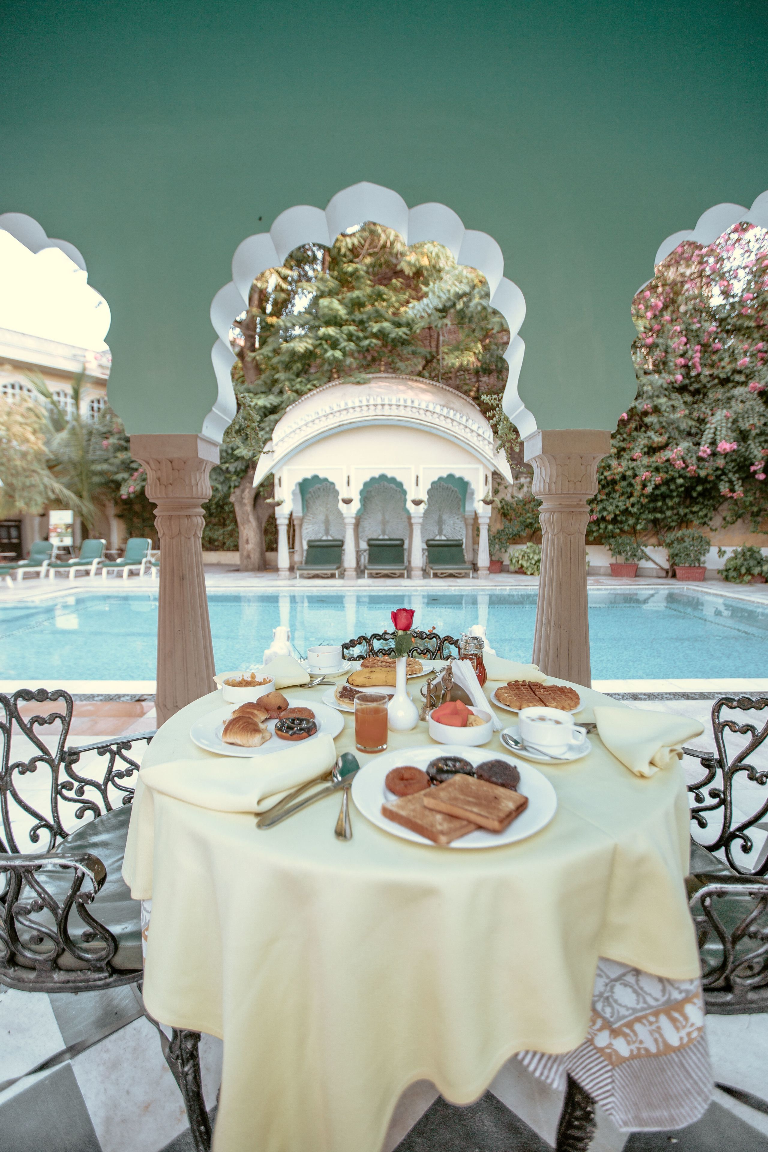 Une table dressée avec des pâtisseries, du thé, et une vue sur une piscine et un jardin.