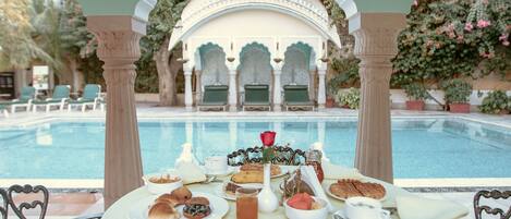 Une table dressée avec des pâtisseries, du thé, et une vue sur une piscine et un jardin.