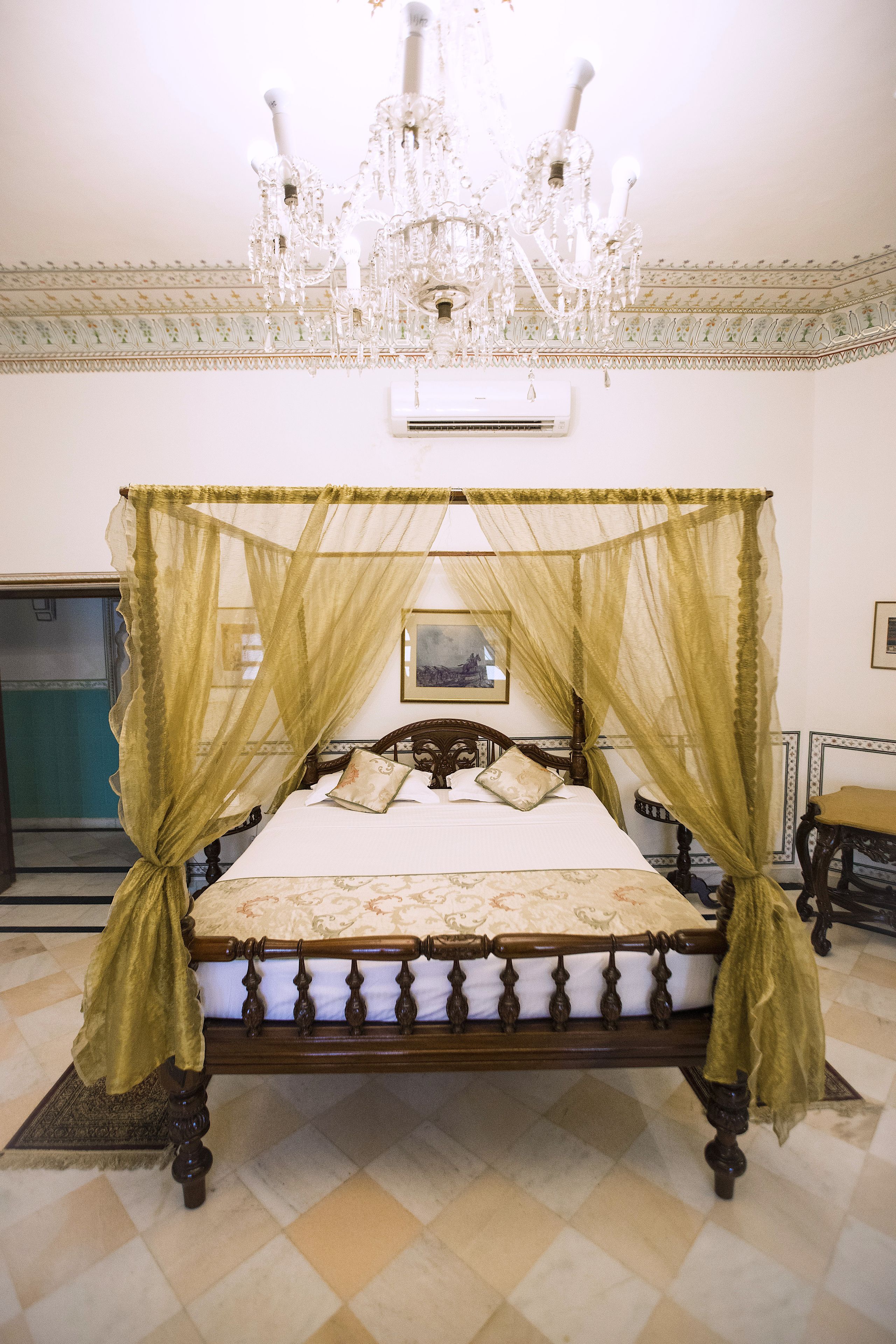 Una cama con dosel, un candelabro y un cuadro en la pared.