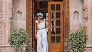 A woman standing at the entrance of a building with ornate carvings and a wooden door. - Alsisar Haveli - A Heritage Hotel (Jaipur)