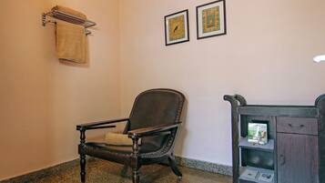 A bathroom with a dark wooden chair, a towel rack with a towel, two framed pictures on the wall, and a small cabinet with a mirror.