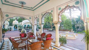 A traditional Indian courtyard with ornate arches, a central fountain, and wicker furniture. - Alsisar Haveli - A Heritage Hotel (Jaipur)
