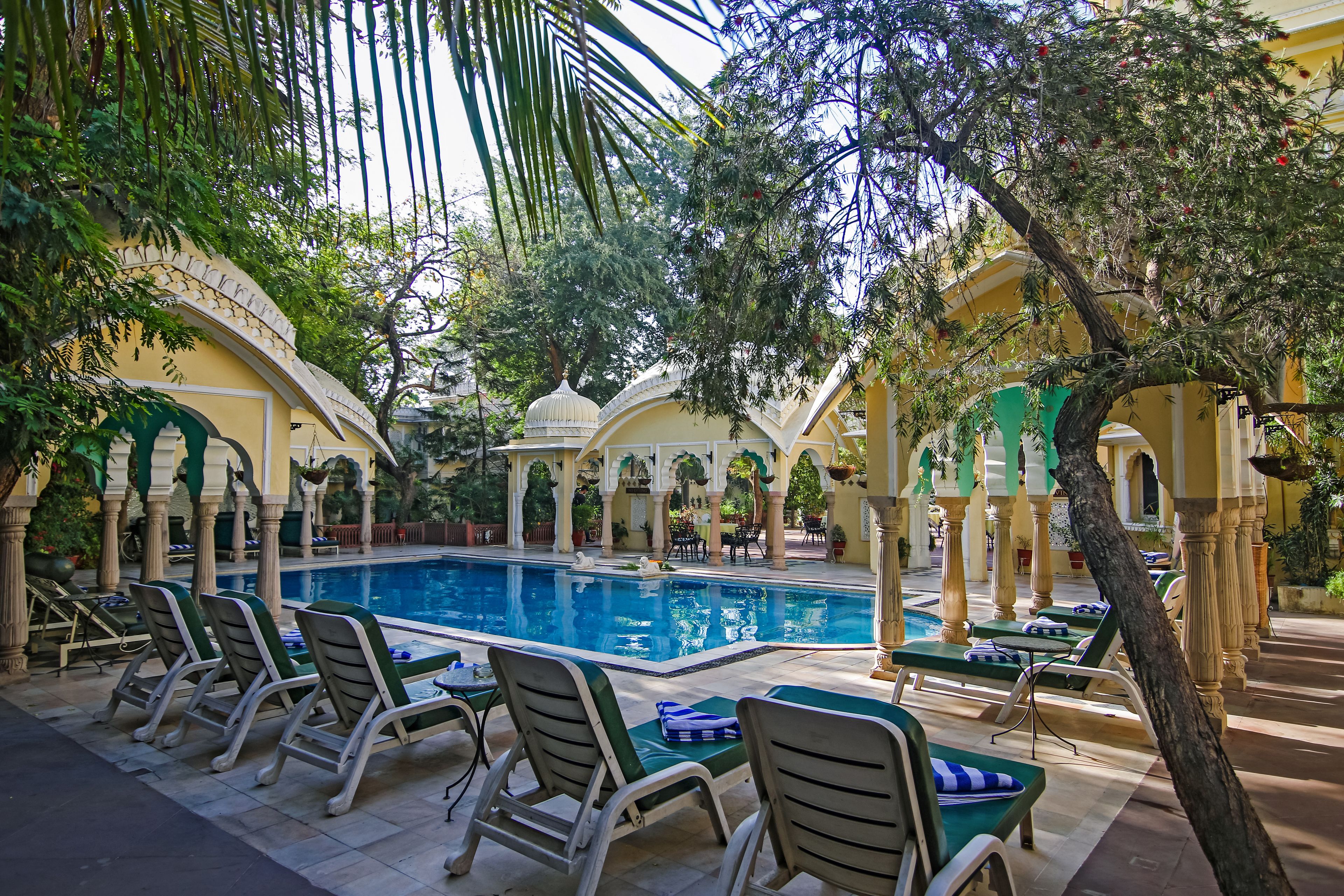 A pool area with lounge chairs and a swimming pool surrounded by arches and trees.