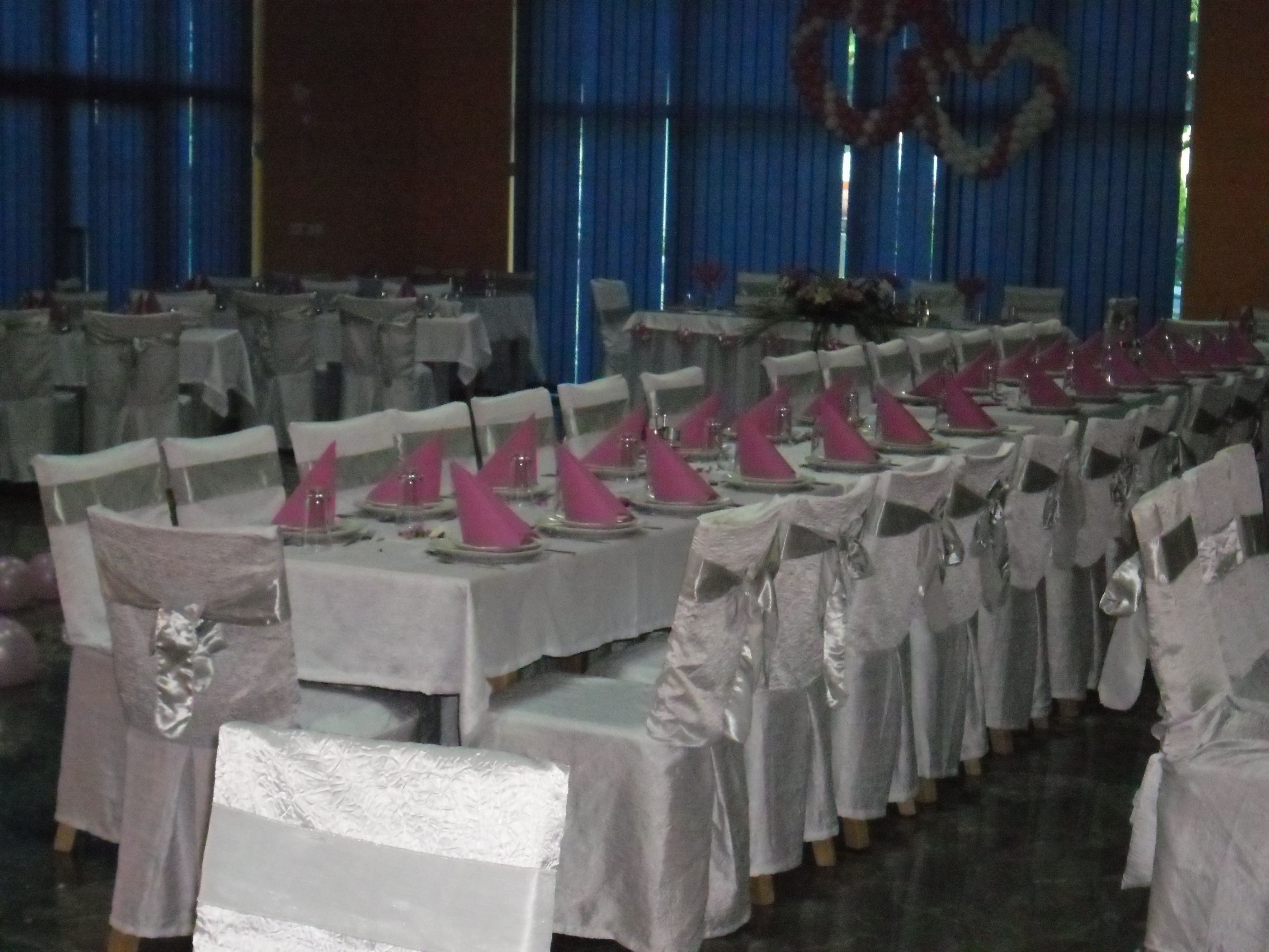 A banquet hall with rows of tables set for a formal event, featuring white tablecloths and chairs with satin sashes.