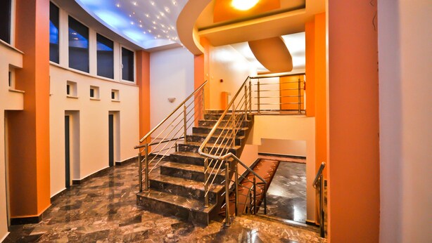 A modern interior with a marble staircase, a ceiling with recessed lighting, and a view of the outside through large windows. - Hotel BM International (Sarajevo)