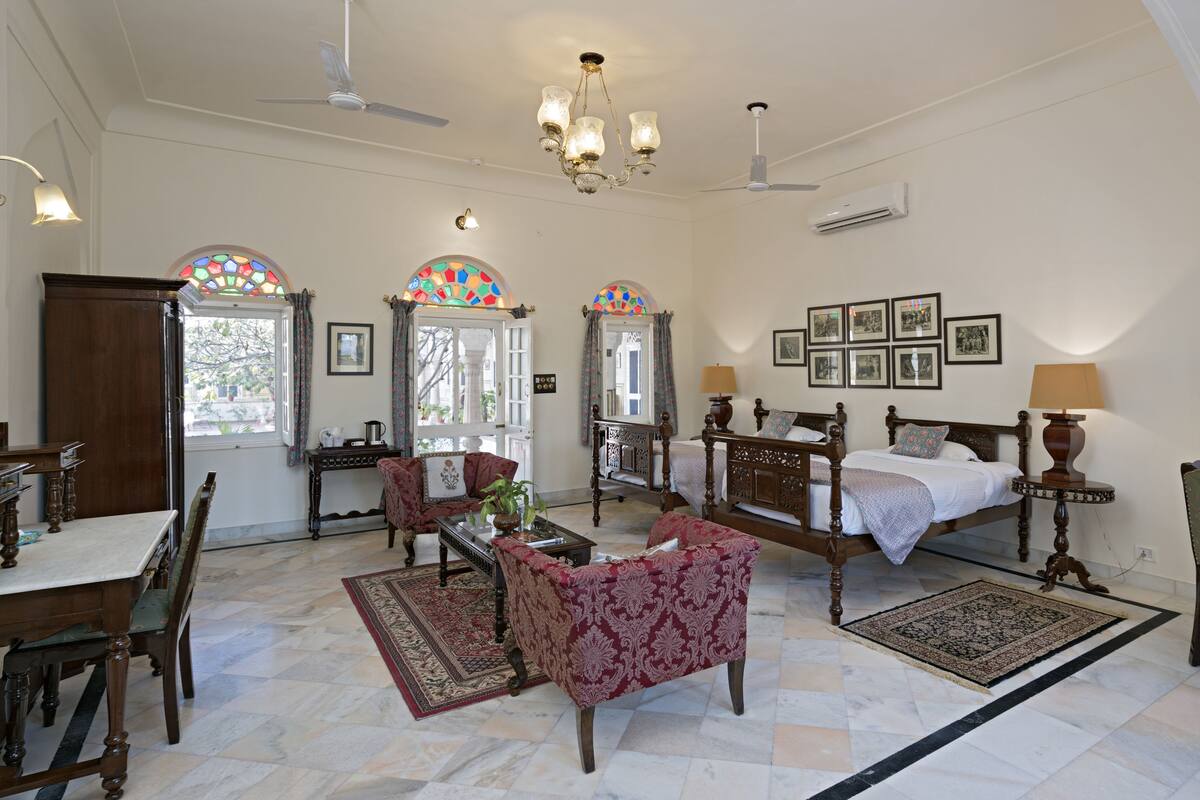 A spacious room with a large bed, two chairs, a table, and a chandelier.
