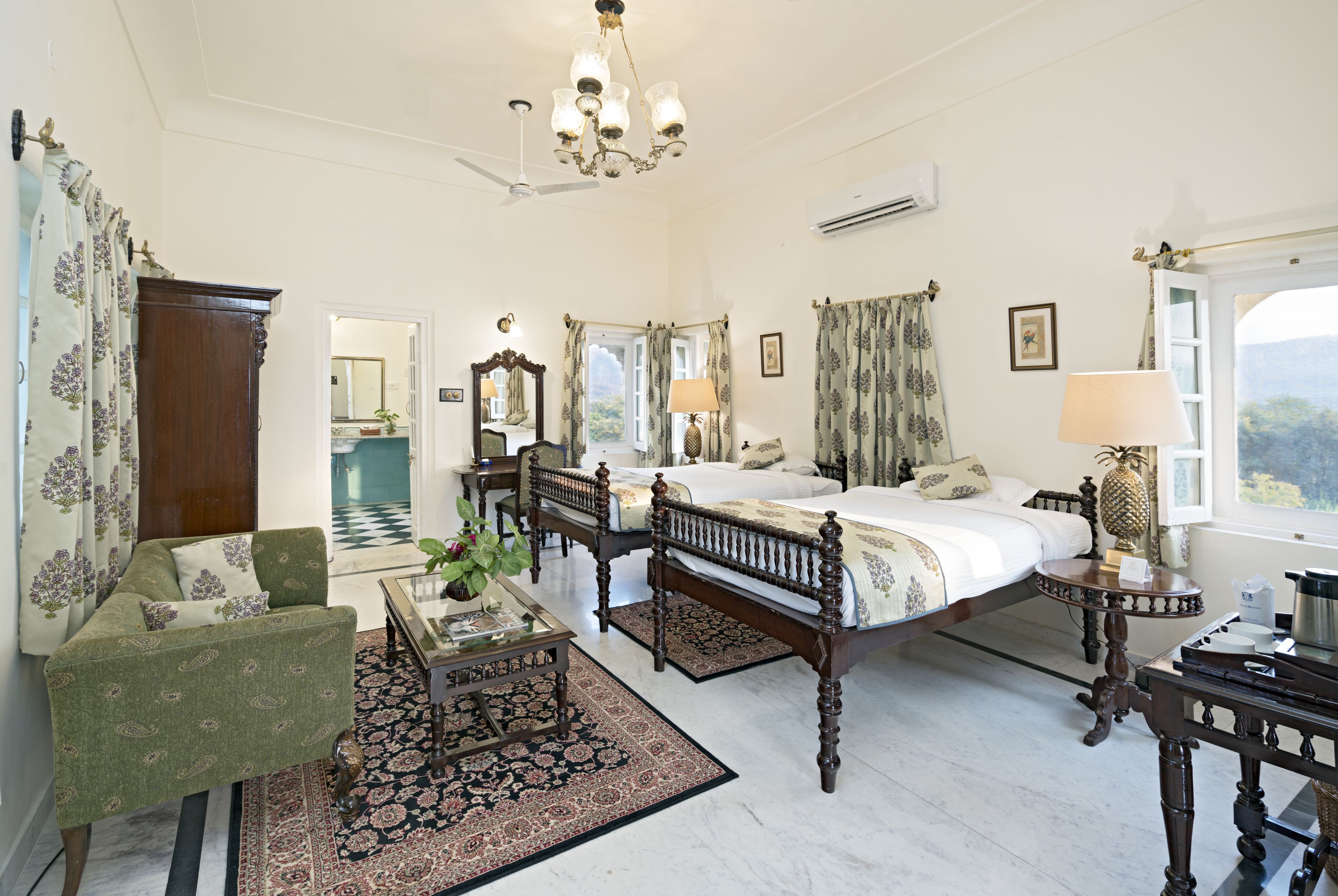 Une chambre à coucher de style traditionnel, avec deux lits, un coin salon comprenant un canapé et une table basse en bois, ainsi qu’une grande fenêtre offrant une vue dégagée.