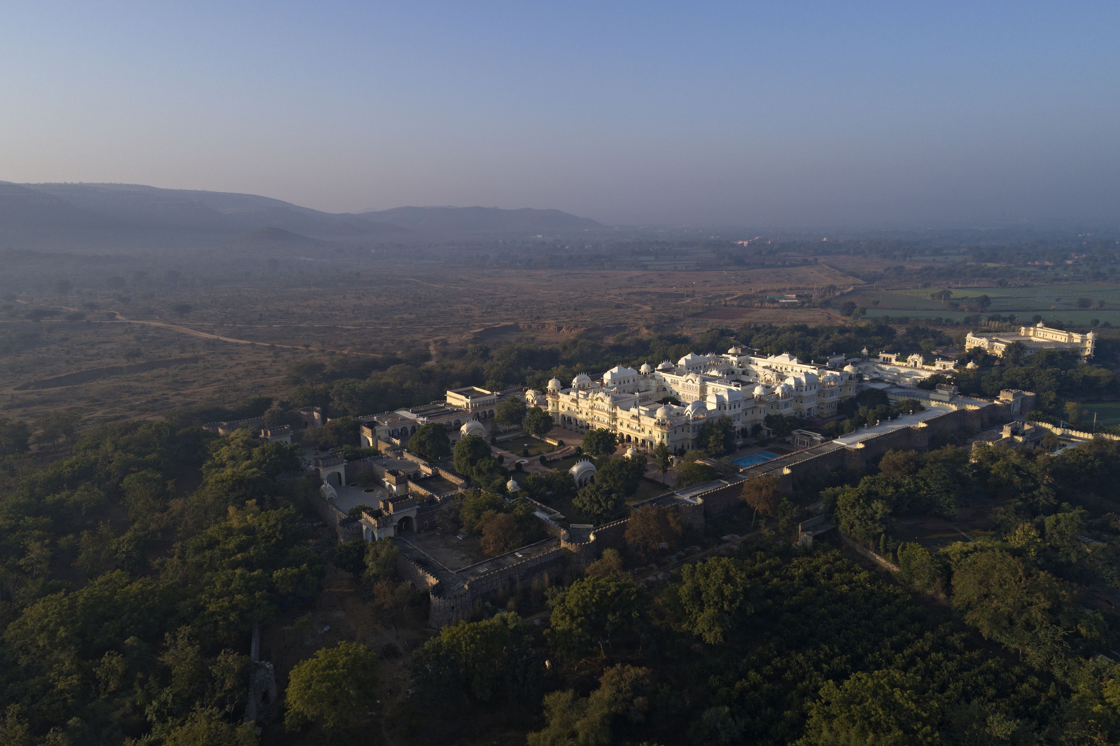 An aerial view of a historic complex with multiple buildings, including a large palace-like structure surrounded by walls and smaller buildings.