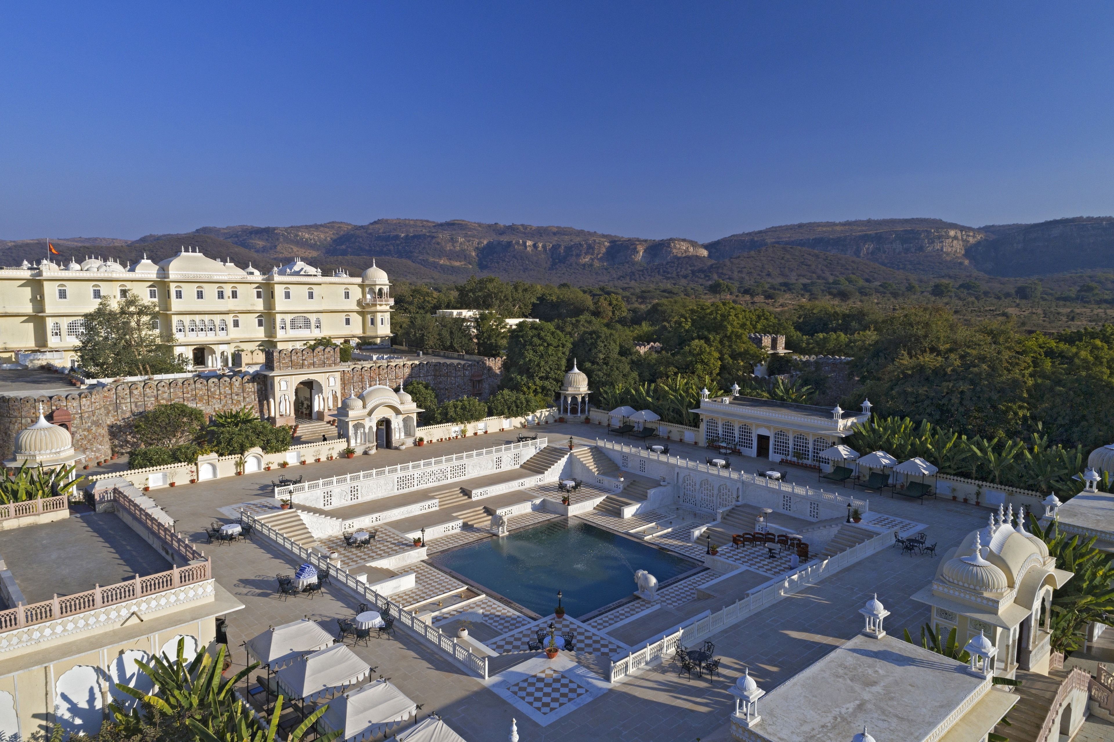 A large, ornate building with a central courtyard, a pool, and a view of surrounding hills.