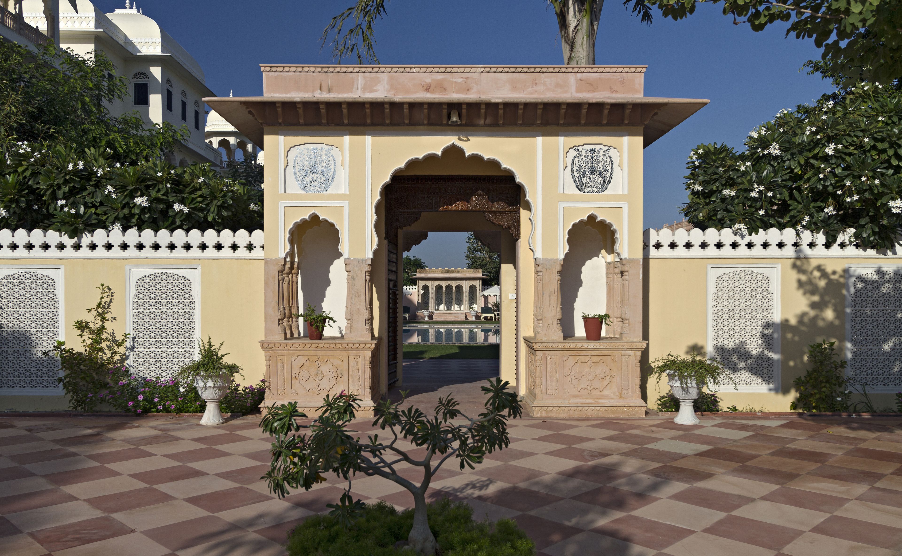 An entrance with ornate arches and a checkered floor, leading to a courtyard with a fountain and potted plants.