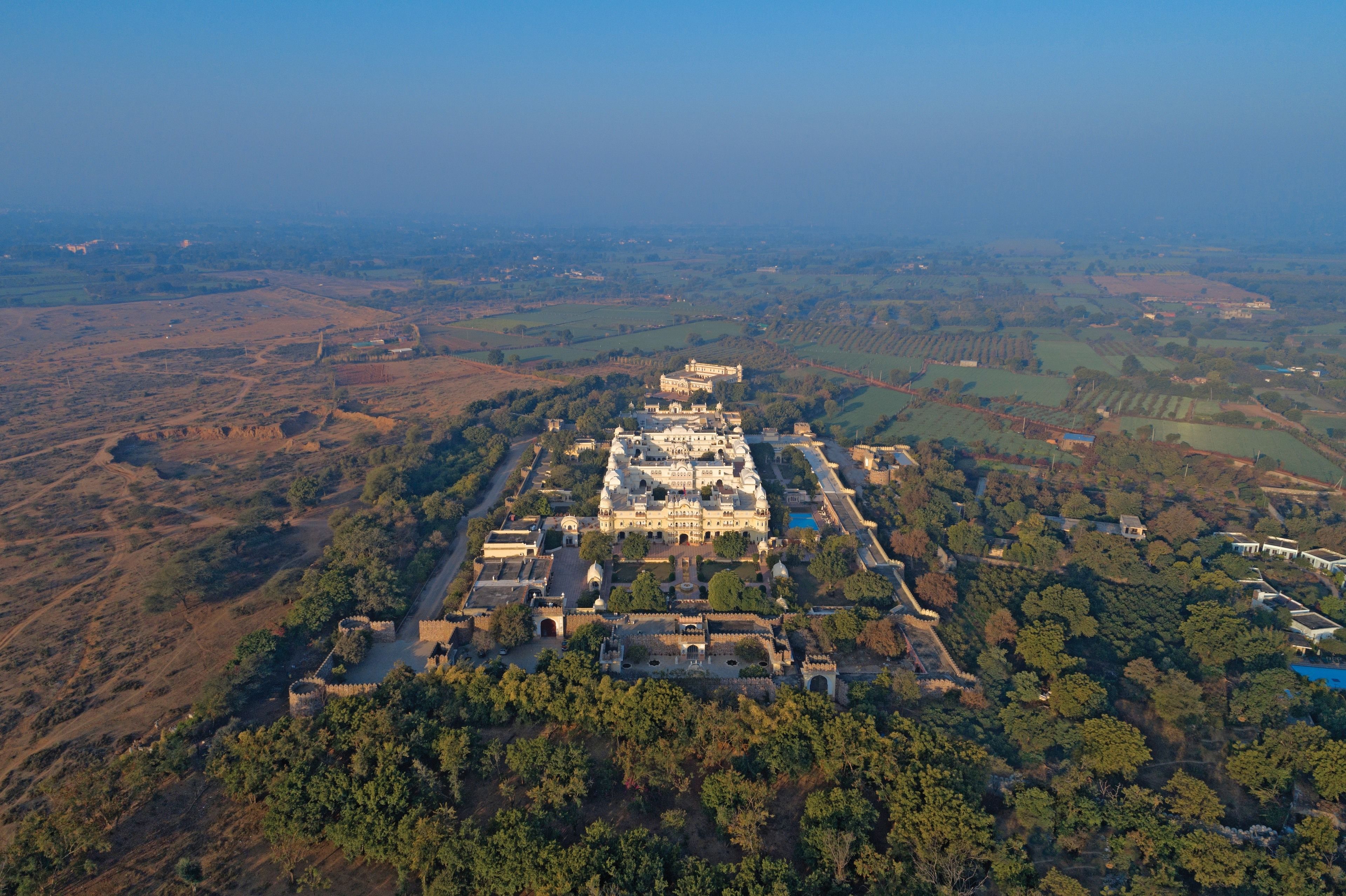 An aerial view of a large, historic building complex surrounded by dense forest and fields.