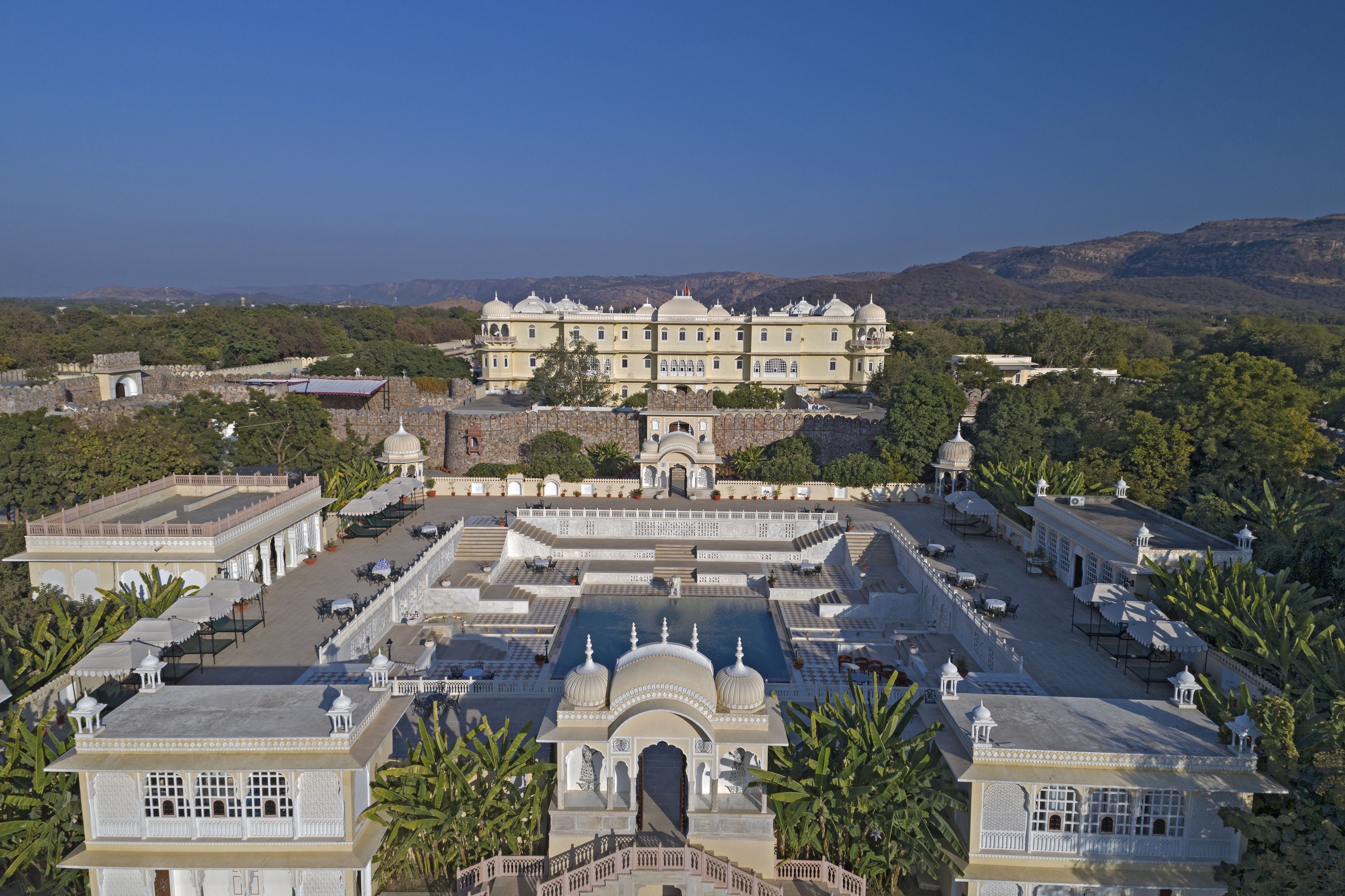 A large, multi-story building with a central courtyard, surrounded by smaller structures and lush greenery.