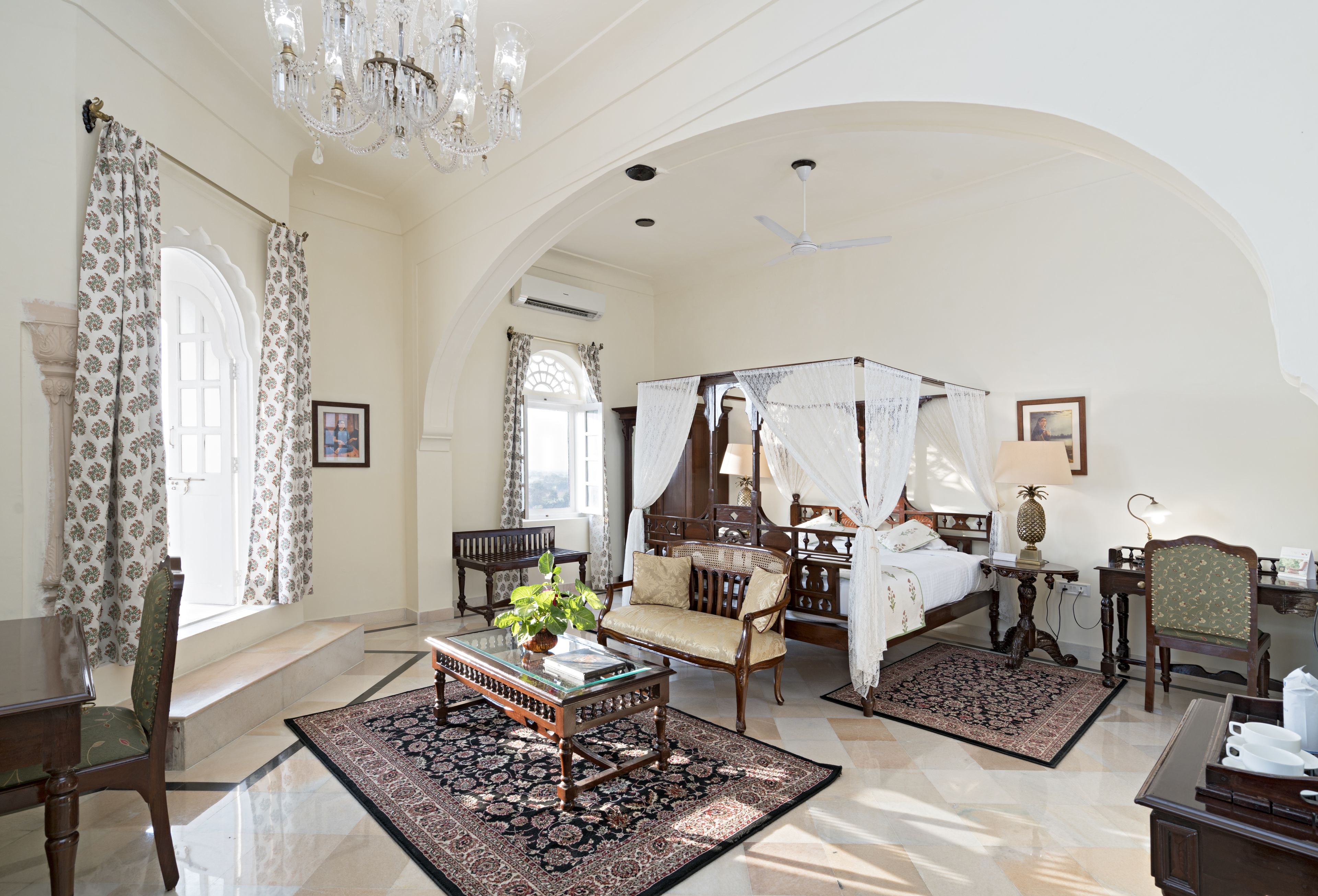 A spacious bedroom with a four-poster bed, a sitting area with a sofa, and a dining table.