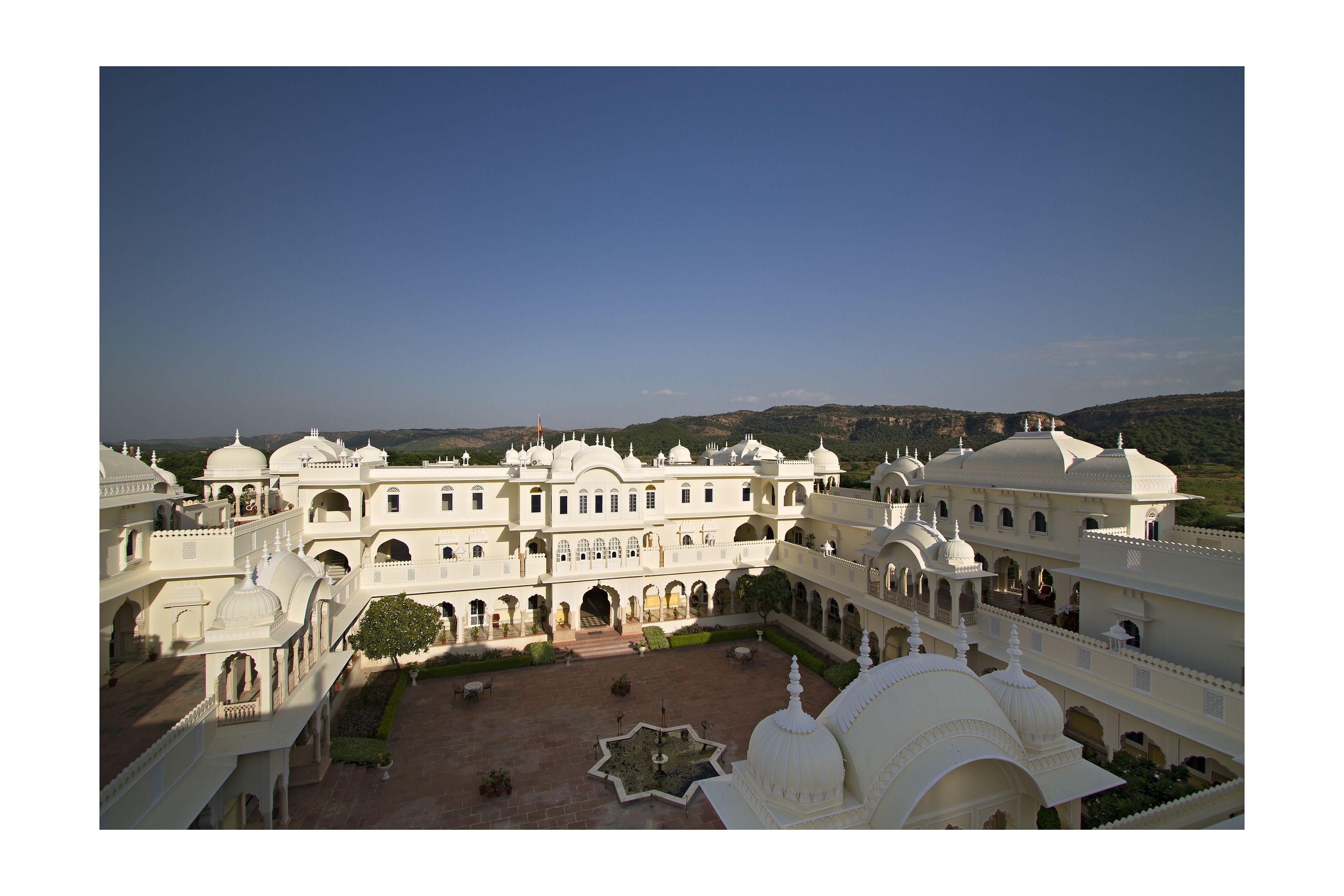 Un grand bâtiment blanc à plusieurs étages, doté de nombreuses coupoles et d’arcades, entouré de cours et de sentiers.