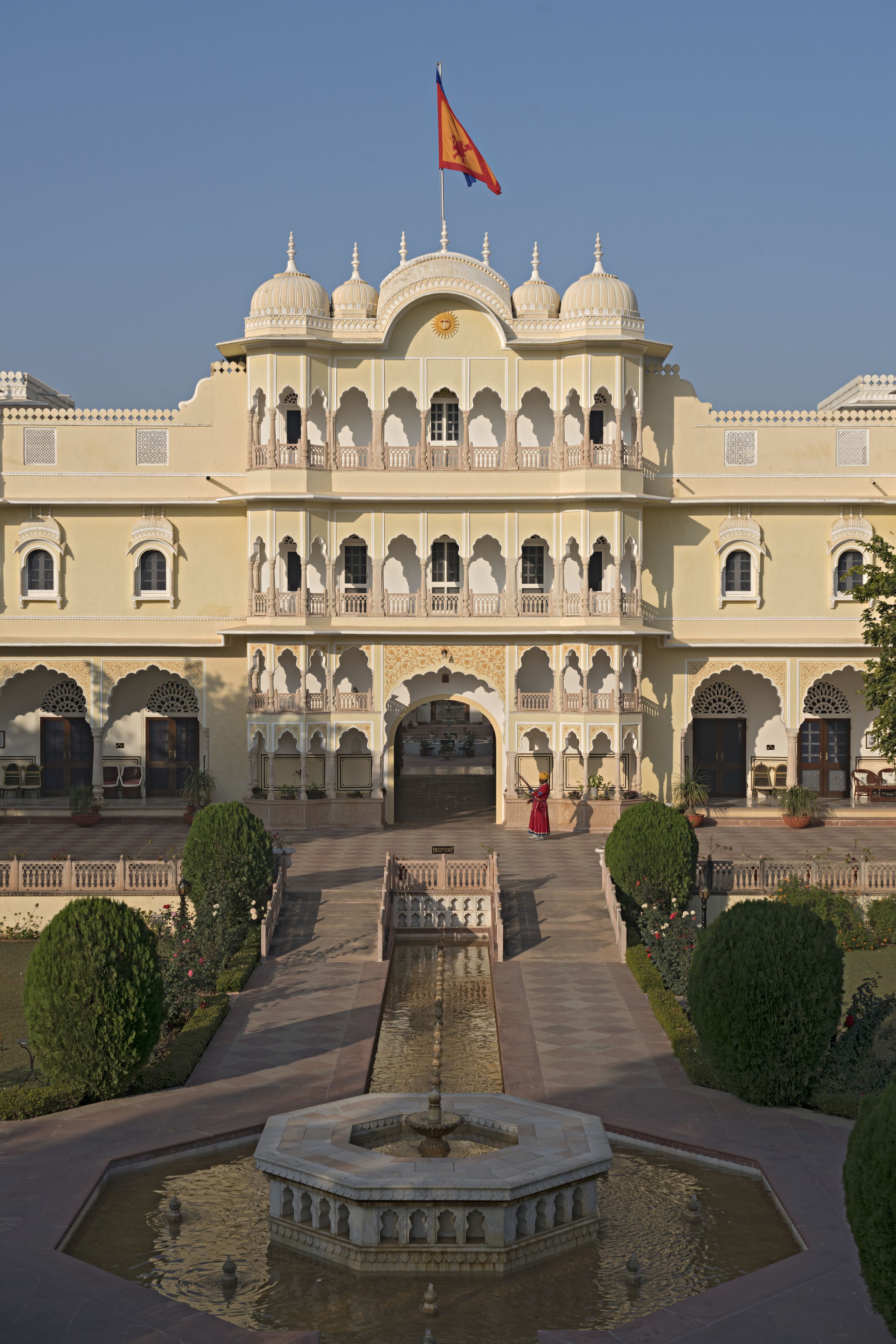A large, ornate building with multiple balconies and arches, a flag on top, and a central fountain.